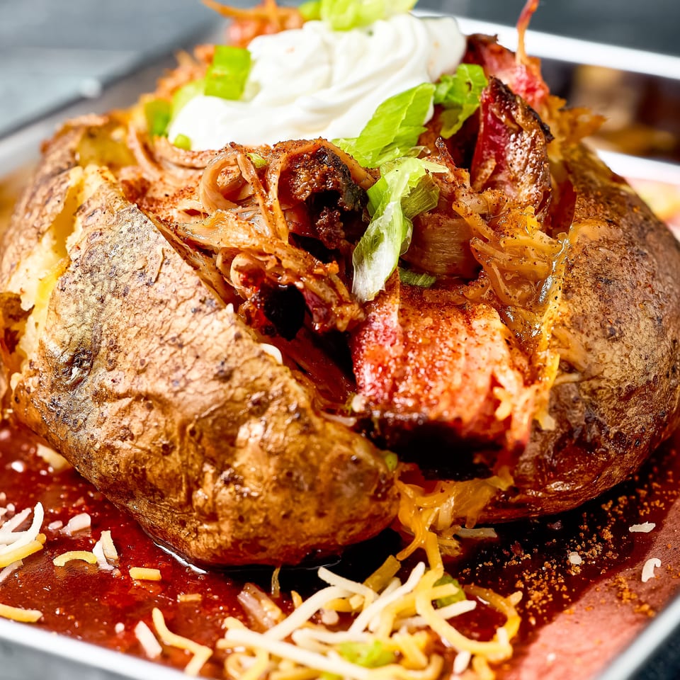 Loaded baked potatoes topped with grilled meat, lettuce, tomatoes, onions, shredded cheese, and sour cream in a tray.