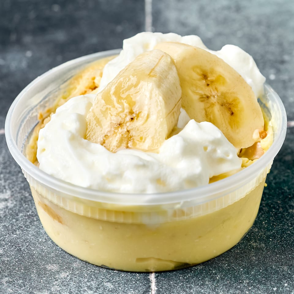 Banana pudding topped with whipped cream and banana slices in a clear container.