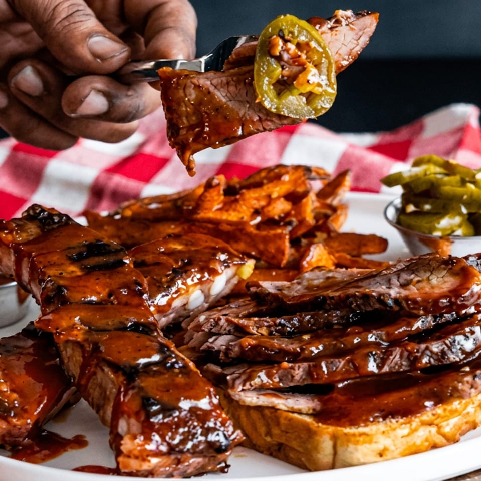 Saucy barbecue ribs and brisket fill a plate with fries, pickles, dipping sauce, and a hand holding a forkful of meat.